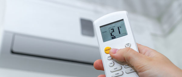 Photo d'une personne actionnant une climatisation avec une télécommande.
